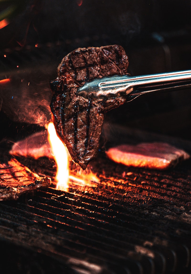 Zange hebt ein Steak über glühende Holzkohle